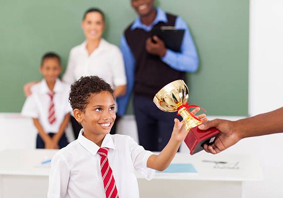 elementary school boy receiving a trophy in classroom with teachers and classmate
